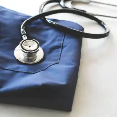Un camice blu e uno stetoscopio appoggiati su un piano bianco. Immagine evocativa per chi vuole capire come diventare guardia medica.