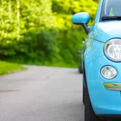 Niemiecki cepik, błękitny Fiat 500, parkuje na krętej drodze wśród zieleni.
