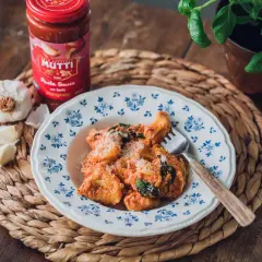 En tallrik med krämig tortellini, toppad med parmesan och färska örter. Bredvid står en burk Mutti tomatsås och vitlök, perfekt för ett enkelt tortellini recept.