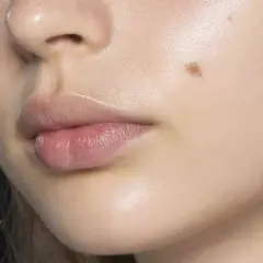 Labios rosados y piel luminosa con un lunar y un ligero vello facial.