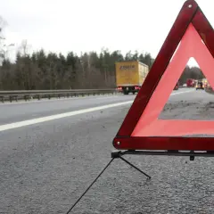 Czerwony trójkąt ostrzegawczy na poboczu drogi, sygnalizujący awarię. W tle ciężarówka i inne pojazdy.