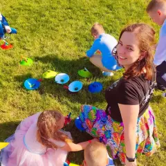 Uśmiechnięta animator dla dzieci cena. Dzieci bawią się na trawie, wykonując zadania z kolorowymi pachołkami.