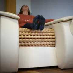 Kobieta relaksuje się na fotelu z masażem rolletic. Drewniane rolki masują jej nogi, podczas gdy ona unosi głowę do góry.