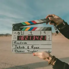 Pustynia, plan filmowy "Roadside". Dwie ręce trzymają klaps z napisem "Jakob & Ryan" i "Thomas Taugher". Opis miejsca.