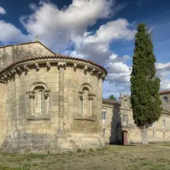 Antigua iglesia románica en Ferreira de Pantón, Lugo. Fachada de piedra con arcos y un ciprés alto.