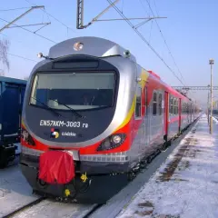 Pociąg EN57AKM-3003 ra z Łodzi stoi na zaśnieżonym peronie. Obok niebieski wagon towarowy.