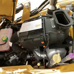 Silnik koparki Cat 428C z widocznym zbiornikiem płynu chłodniczego i wlewem oleju hydraulicznego.
