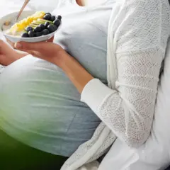 Schwanger mit Eisenmangel? Eine junge Frau liest und isst Obstschale, um sich zu stärken.