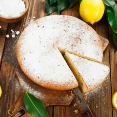 Un délicieux gâteau italien au limoncello, saupoudré de sucre glace, avec des citrons frais et des feuilles vertes sur fond de bois.