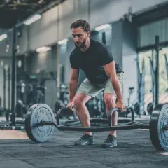 Un homme concentré effectue un dead lift avec une barre hexagonale dans une salle de sport.