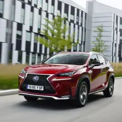 Czerwony Lexus NX, uznawany za najbardziej ekonomiczny SUV, jedzie przed nowoczesnym budynkiem.
