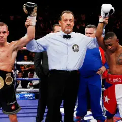 Referee raises the winner's hand after a boxing match. The boxer on the left, wearing a championship belt, achieved a win by decision.