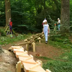 Ein Mädchen erkundet den erlebnispfad eifel kinder. Holzrinnen und eine Spielzeugbahn schlängeln sich durch den Wald.