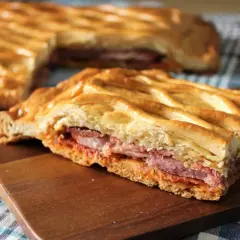 Un delicioso hornazo de Pascua, con su masa dorada y relleno de carnes, listo para compartir.