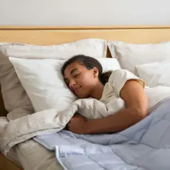 Joven durmiendo plácidamente, quizás gracias a la melatonina, envuelta en mantas y almohadas blancas.