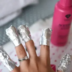 Dłonie z paznokciami owiniętymi folią aluminiową, gotowe do usunięcia lakieru. Obok różowa butelka z acetonem. Czas oczekiwania?