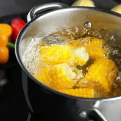 Kukurydza na ryby gotuje się w garnku. W tle pomarańczowa i czerwona papryka.