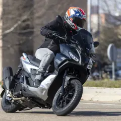 Motorista con casco a bordo de una Aprilia SR GT 125, lista para alcanzar su velocidad máxima en la carretera.