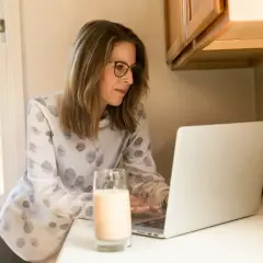 Frau mit Brille am Laptop, studieren mit 40 berufschancen. Ein Glas Milch steht daneben.