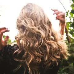 Cabello rubio con reflejos naturales, como si fuera babylights vs balayage. Manos en el aire, rodeada de vegetación.