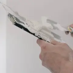 Händer spacklar på en vit vägg, förbereder för tapetsering.