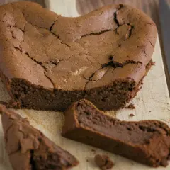 Un délicieux gâteau au chocolat en forme de cœur, un gâteau sans oeuf, craquelé sur le dessus, avec une part coupée.
