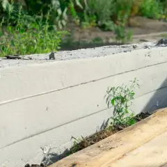 Solidny fundament pod ogrodzenie, z widocznymi poziomymi liniami i zielenią przebijającą się z ziemi.