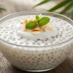 Un bol de tapioca au lait de coco, garni de copeaux de noix de coco et d'une feuille de menthe.