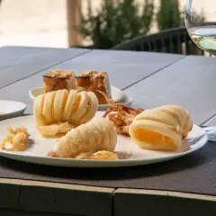 Deliciosa fritura de pescado, calamares crujientes y anillas de calamar, acompañados de pan tostado y una copa de vino blanco.