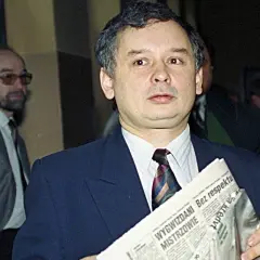 Jarosław Kaczyński, jeden z tych, kto założył PiS, trzyma gazetę. Obok stoi mężczyzna w okularach.