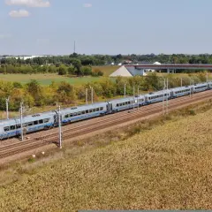 Nowoczesny pociąg Pendolino pędzi po magistrali kolejowej, mijając pola kukurydzy i zielone drzewa.