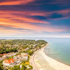 Ein perfekter tagesausflug ostsee: Sonnenuntergang über der Ostsee, belebter Strand mit Liegen und ein Küstenort mit roten Dächern.