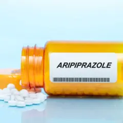 Pomarańczowa butelka z tabletkami, na etykiecie napis Aripiprazol. Kilka białych tabletek rozsypanych obok.