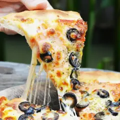 Ciągnący się ser z kawałka pizzy capriciosa z oliwkami, podnoszony ręką.