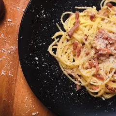 Un plat de spaghetti à la carbonara, garni de lardons et de parmesan râpé, prêt à être dégusté. Parfait pour des recettes pâtes à la carbonara.