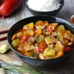 Sabroso wok de cerdo con trozos de piña, pimientos rojos y verdes, servido en un cuenco negro.