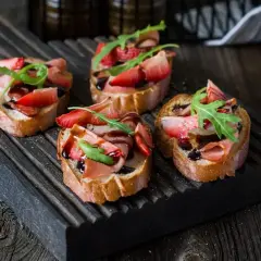 Bruschetta z truskawkami i szynką prosciutto, polana balsamicznym sosem. Idealny przepis na letnią przekąskę.