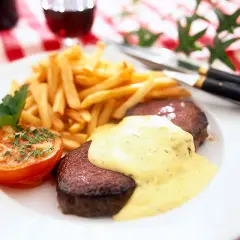 En tallrik med saftig steak frites, gyllene pommes frites, en ugnsbakad tomat och en krämig sås. En klassisk måltid!