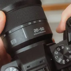 Dłonie trzymają aparat, obracając pierścień z oznaczeniami 20-60 mm. To właśnie zoom, czyli możliwość zmiany ogniskowej obiektywu.