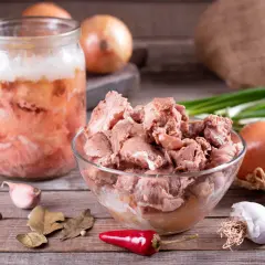 Słoik z domowym mięsem, jak u babci, pełen smaku. Obok miska z porcjami mięsa, cebula, czosnek, papryczki chili i przyprawy.