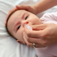 Mani che aiutano un neonato di 2 mesi con la tosse, somministrando gocce nasali per alleviare il naso chiuso.