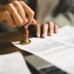Dłoń trzymająca pieczęć notarialną nad dokumentem.
