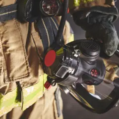 Bombero con equipo de protección, incluyendo una máscara y un compresor de aire respirable.