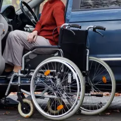 Osoba w wózku inwalidzkim obok otwartych drzwi samochodu. Wózek jest gotowy do podróży, zapewniając ulgę na samochód i mobilność.