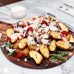 Biff Tagliata with roasted potatoes, tomatoes, pine nuts, parmesan, and arugula on a wooden board.
