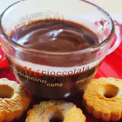 Bicchiere di cioccolata calda con acqua senza fecola, accompagnata da biscotti su un piatto rosso.
