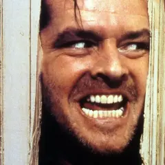 Jack Nicholson, con occhi bianchi e sorriso folle, sfonda una porta. Il suo volto è il **shining significato finale** di un incubo.