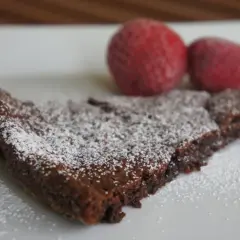 En bit kladdkaka, pudrad med florsocker, med två jordgubbar i bakgrunden. Perfekt för dig som älskar kladdkakecookies utan choklad.
