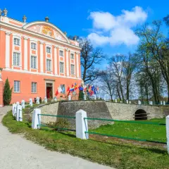 Pałac w Kurozwękach, z licznymi flagami przed wejściem, zaprasza do odkrywania jego atrakcji.