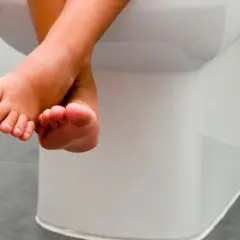 Kleine Füße baumeln über der Toilette. Tipps, wie Kinder trocken werden, sind hier wichtig.